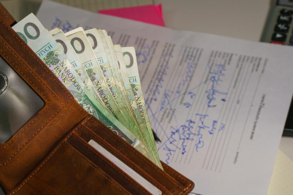 Close-up of a wallet containing Polish Zloty with a signed document in the background, representing